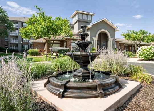 Decorative fountain and landscaped entrance outside the clubhouse and leasing office at The Claremont Apartments in Overland Park, KS.