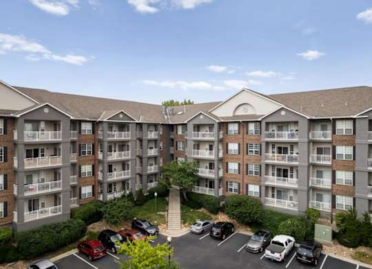 Courtyard parking area surrounded by multi-story apartment buildings with private balconies at The Claremont Apartments in Overland Park, KS.