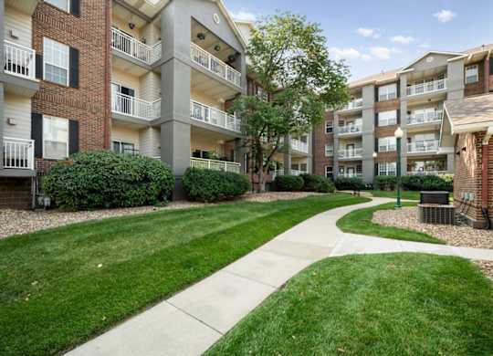Landscaped pedestrian walkway between apartment buildings at The Claremont Apartments featuring manicured lawns and mature trees in Overland Park, KS.
