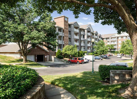 View of residential apartment buildings, parking area, and mature shade trees throughout The Claremont Apartments community in Overland Park, KS.