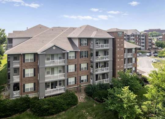 Exterior view of a residential apartment building with private balconies and mature landscaping at The Claremont Apartments in Overland Park, KS.