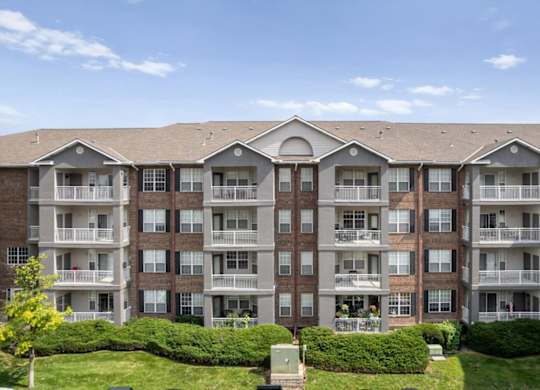 Multi-story apartment building exterior featuring private balconies, landscaped green space, and well-maintained grounds at The Claremont Apartments in Overland Park, KS.