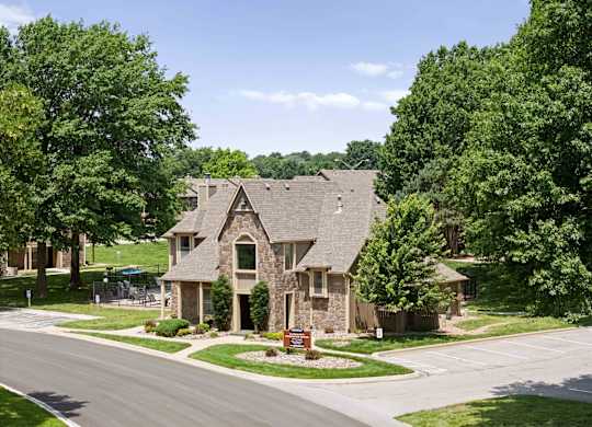 A house with a stone facade is surrounded by green trees.