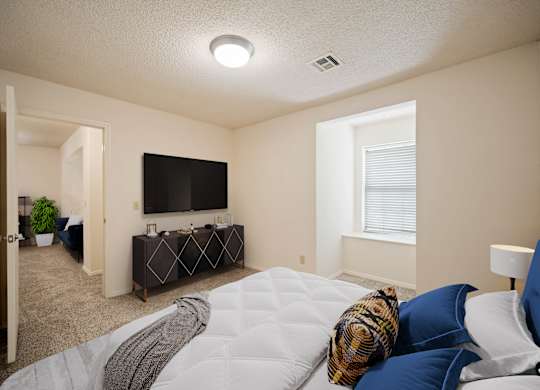 A bedroom with a bed, a couch, a television, and a window.