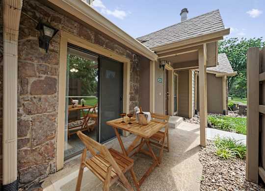 A wooden table and chairs are on a patio outside a house.