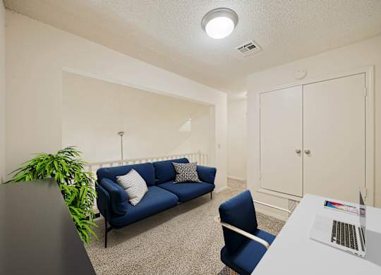 A room with a blue couch, a white desk, and a laptop on it.