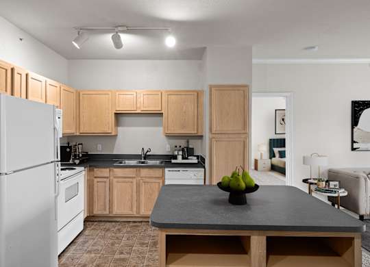 A kitchen with oak cabinets, white appliances, track lighting and a kitchen island with storage.