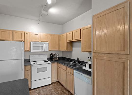 A kitchen with oak cabinets, white appliances, track lighting and a kitchen island with storage.