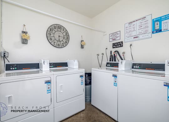 A laundromat with a clock on the wall and machines with stickers on them.