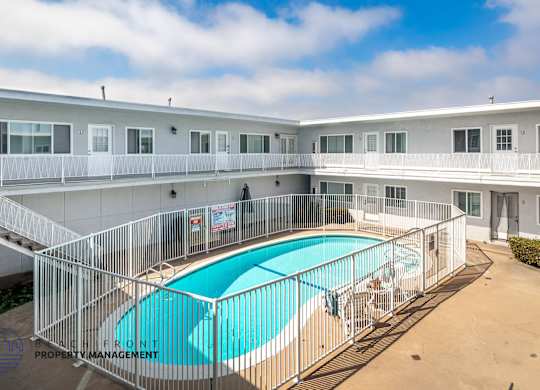 A pool surrounded by a fence in a sunny courtyard.
