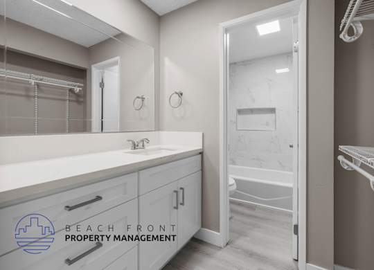 A bathroom with a sink, mirror, and a logo for Beach Front Property Management.
