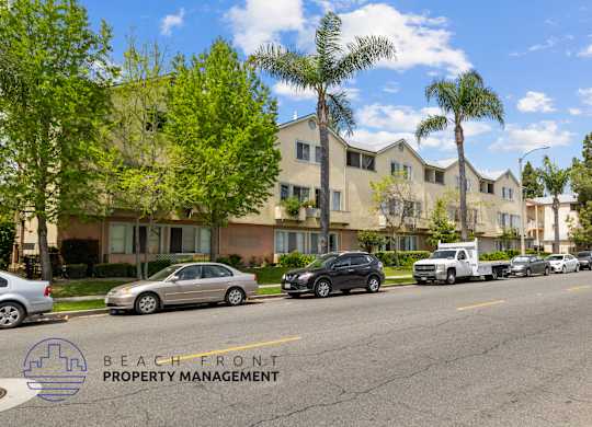 A street view of a residential area with cars parked on the side of the road and apartment buildings in the background.