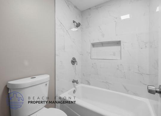 A white bathroom with a marble wall and a toilet with a logo that says Beach Front Property Management.