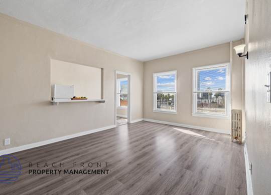 A spacious room with wooden flooring and a view of K-town through the windows.