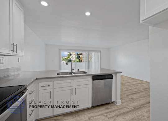 A kitchen with a sink and cabinets with a window in the background.