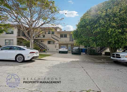 A white car is parked in front of a building with the logo of Beach Front Property Management.