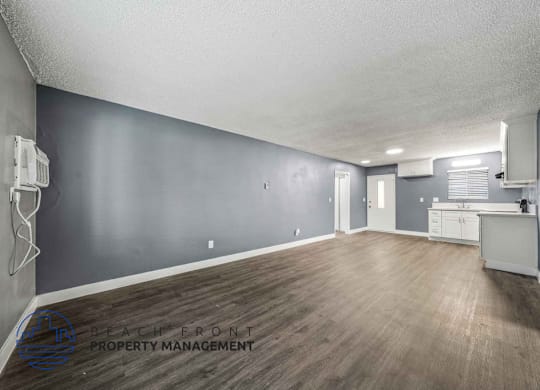 A spacious room with wooden flooring and a kitchenette in the background.