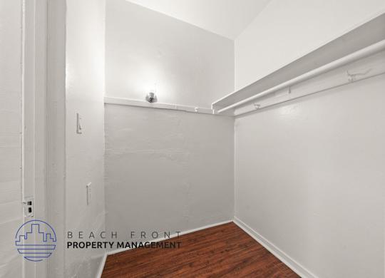 A white room with a wooden floor and a white wall with a pipe running along it.