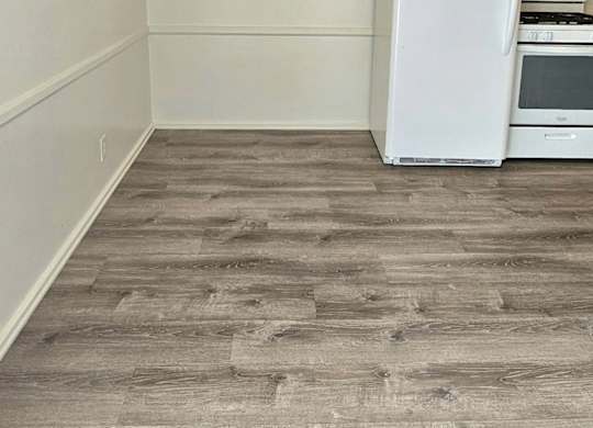 A white fridge in a room with wooden flooring.