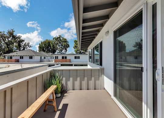 A wooden bench is on a patio with a glass door.
