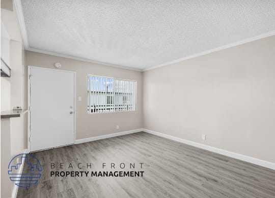 the spacious living room of an apartment with wood flooring and a door to the