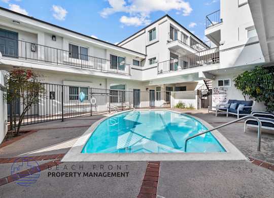 A pool surrounded by a patio with chairs and a building in the background.