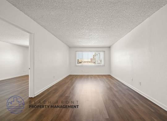 A room with wooden floors and white walls, with a window showing a beach scene.