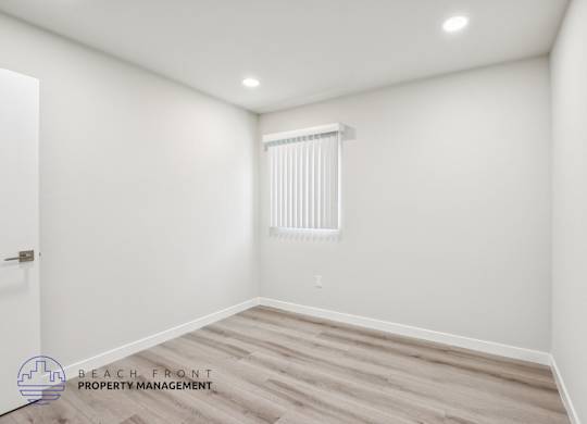 A room with a wooden floor and a window with blinds.