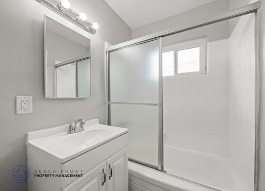 A white bathroom with a sink, mirror, and shower.