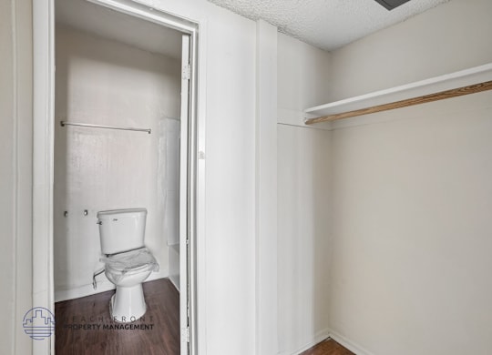 A white toilet is in a small bathroom with a wooden floor.
