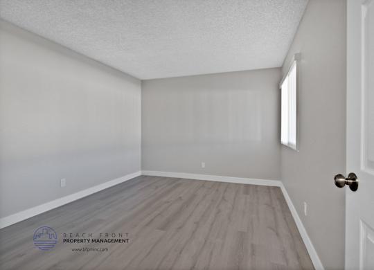 A room with a wooden floor and white walls, with a door on the right side.
