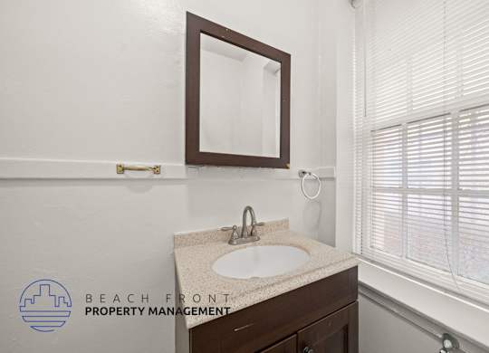 A bathroom with a sink, mirror, and window with blinds.