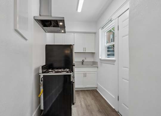 A black stove is in a white kitchen with wood floors.