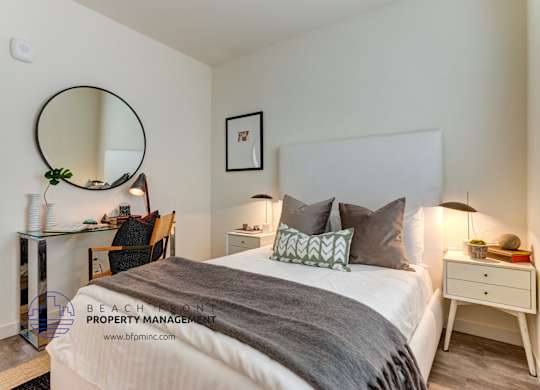 A bedroom with a large bed, a desk with a chair, a mirror, and a lamp.