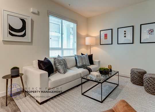 A living room with a white couch, a glass coffee table, and a window with blinds.