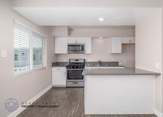A kitchen with white appliances and cabinets, a window with blinds, and a logo for Beach Front Property Management.