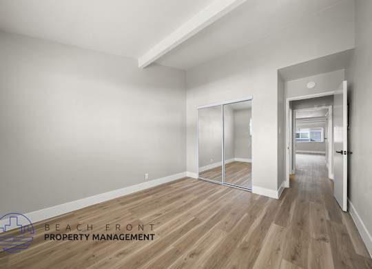 A spacious room with wooden flooring and a logo for Beach Front Property Management in the corner.
