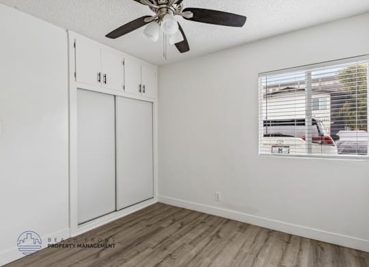 A room with a ceiling fan and a window showing a view of a parking lot.