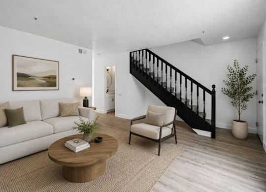 A living room with a white couch, a wooden coffee table, a chair, a potted plant, and a painting on the wall.