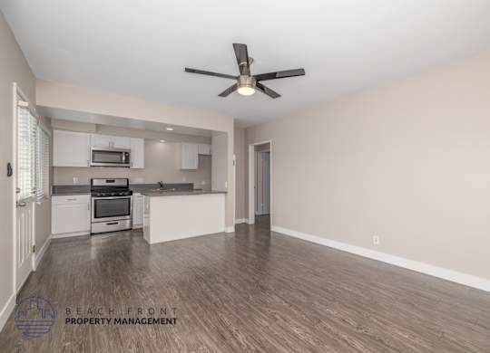 A spacious room with a fan and wooden flooring.
