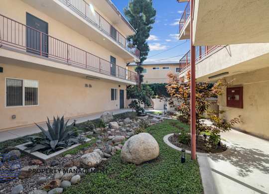 A courtyard with a rock in the middle and a tree on the right.