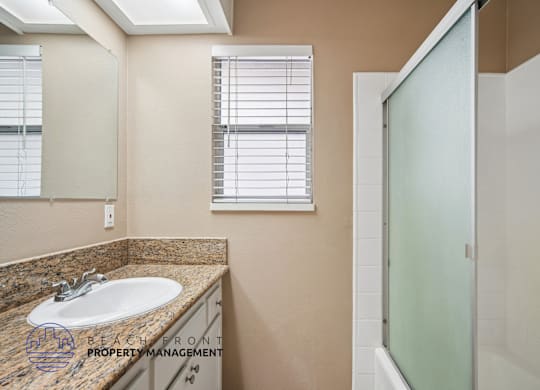 A bathroom with a sink, mirror, and shower.