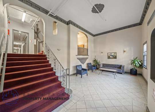 A staircase with a metal railing leads to a landing with a couch and two chairs.