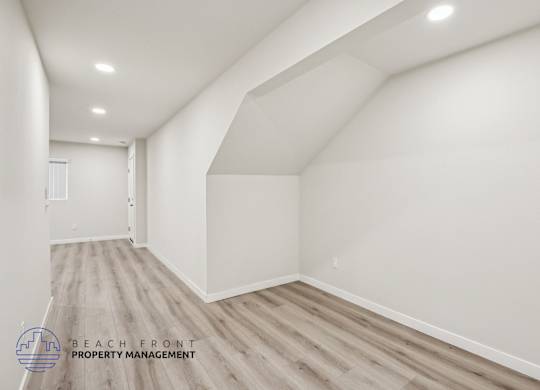 A spacious room with wooden flooring and white walls, managed by Beach Front Property Management.