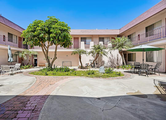 A courtyard with a tree, chairs, and a table is surrounded by buildings.