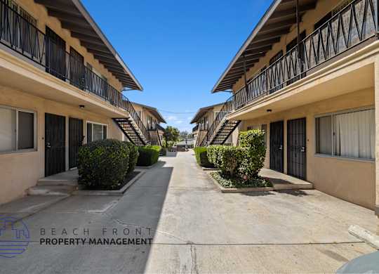 a long walkway between two buildings with balconies and bushes