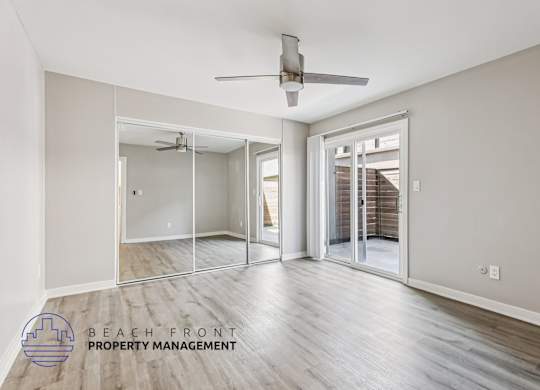 A spacious room with a ceiling fan and sliding glass doors leading to a balcony.