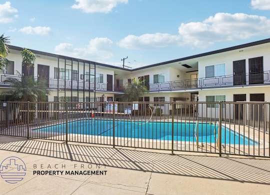 A pool surrounded by a fence and a building with balconies.