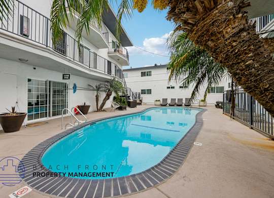 A pool surrounded by a fence and a building with a balcony.