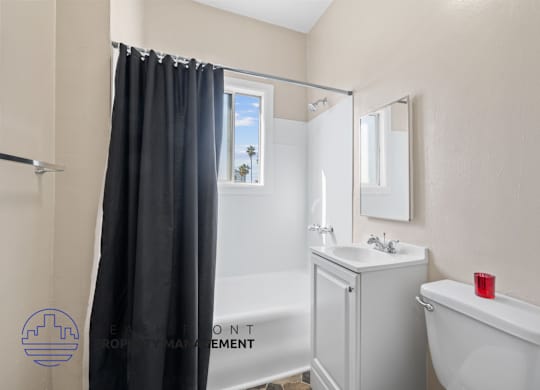 A bathroom with a white tub, sink, and a window with a black curtain.